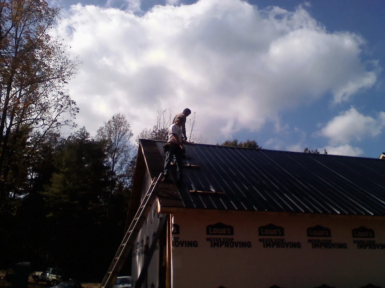 Roofer fastening dark metal panels high against a cloudy sky, from a Roof Inspection job in Mount Hermon